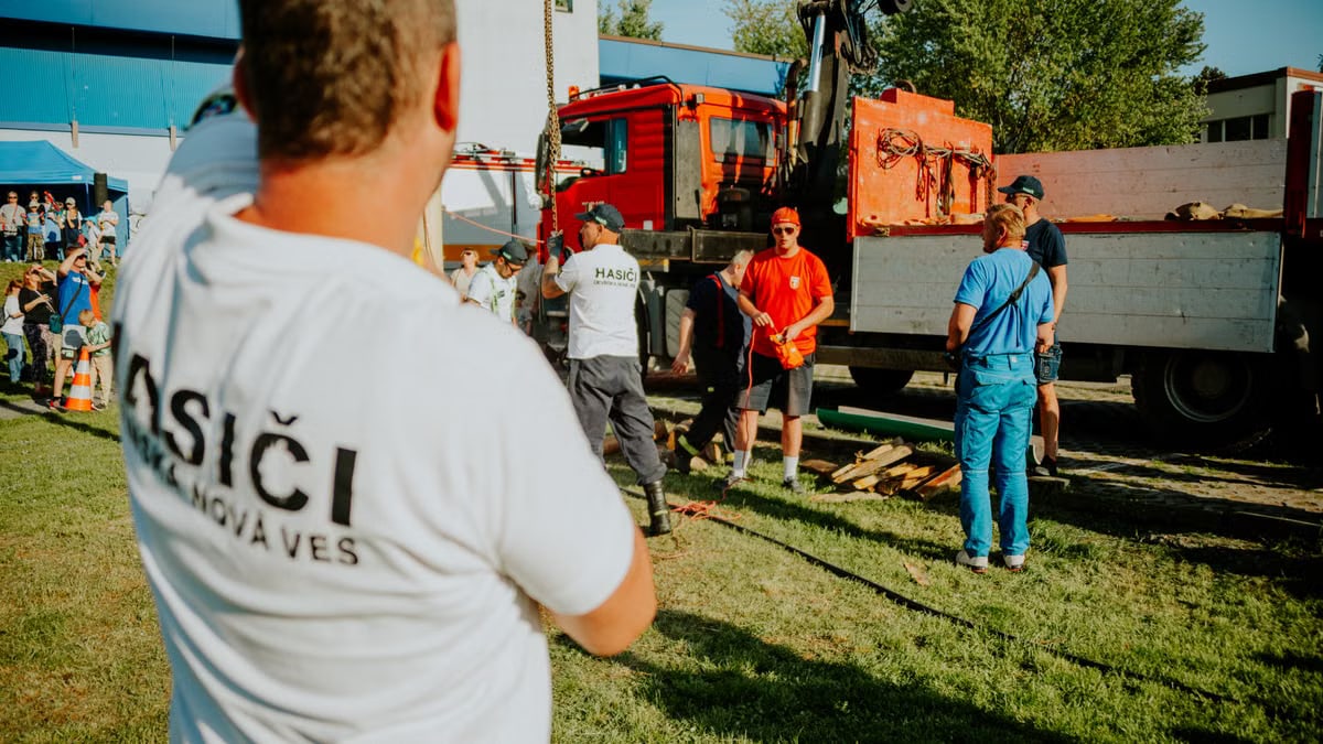 A group of firefighters in a park setting during a public demonstration near a fire truck.